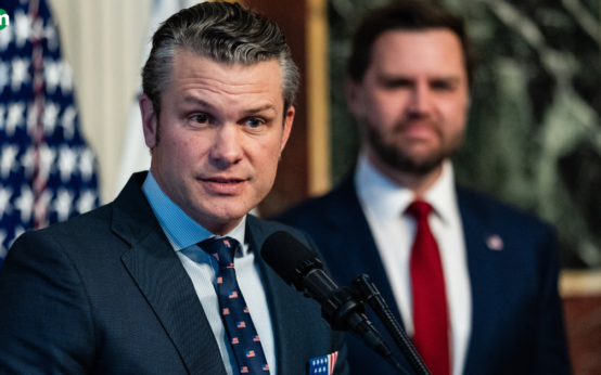 Pete Hegseth speaking at an event with an American flag in the background